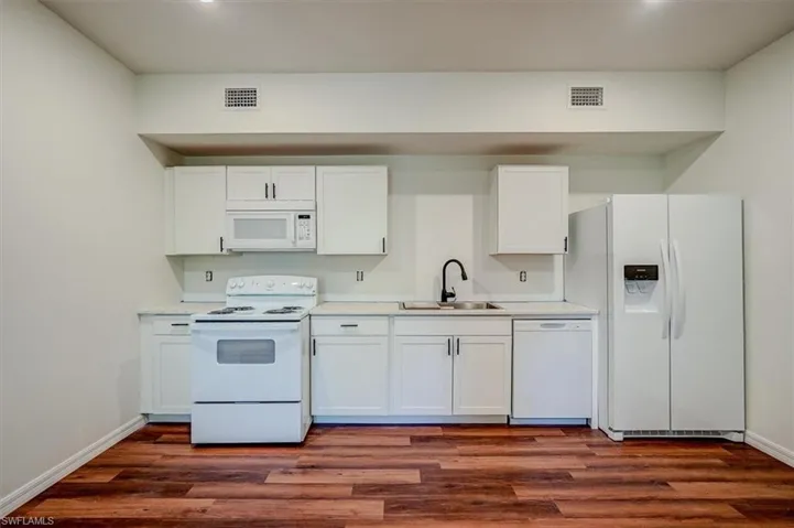 Kitchen with white cabinets, a sink, white appliances, and light countertops