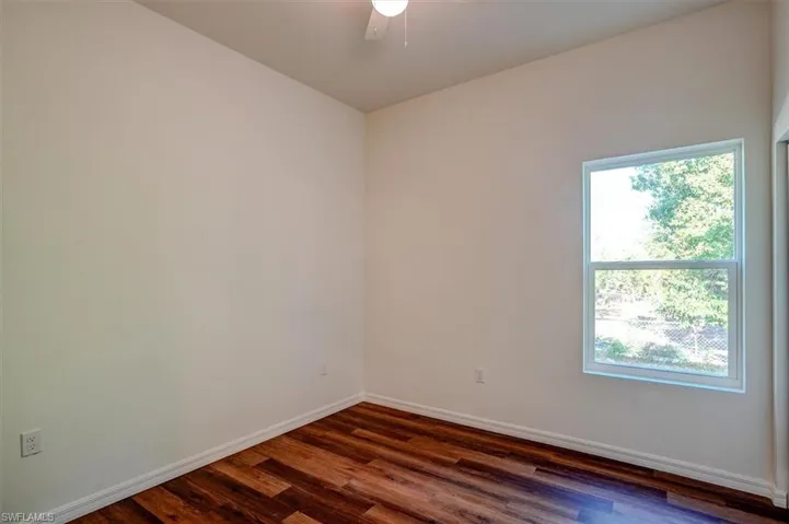 Empty room featuring dark wood finished floors, baseboards, a ceiling fan, and plenty of natural light