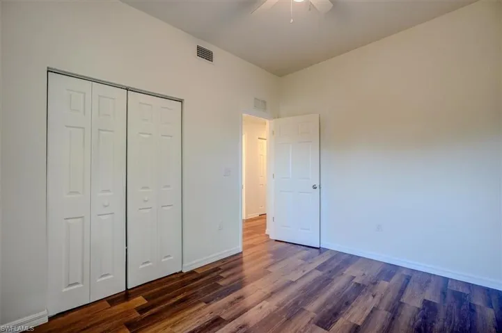 Unfurnished bedroom with baseboards, visible vents, dark wood-style floors, and a closet