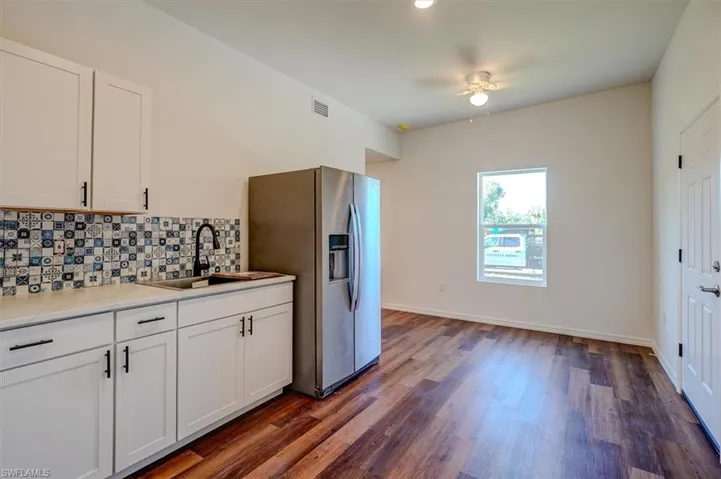Kitchen featuring white cabinets, a sink, tasteful backsplash, stainless steel refrigerator with ice dispenser, and dark wood-style flooring
