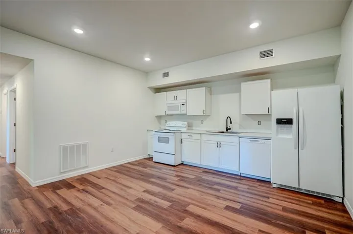 Kitchen with visible vents, wood finished floors, white appliances, and a sink
