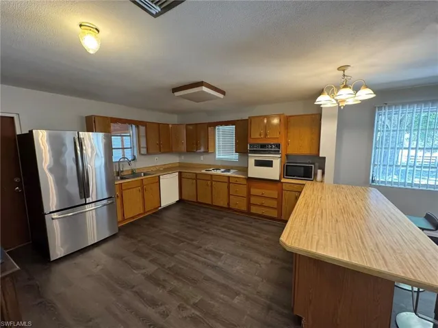 Kitchen with a peninsula, white appliances, a sink, light countertops, and decorative light fixtures