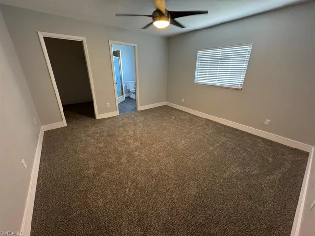 Empty room featuring ceiling fan, baseboards, and dark colored carpet