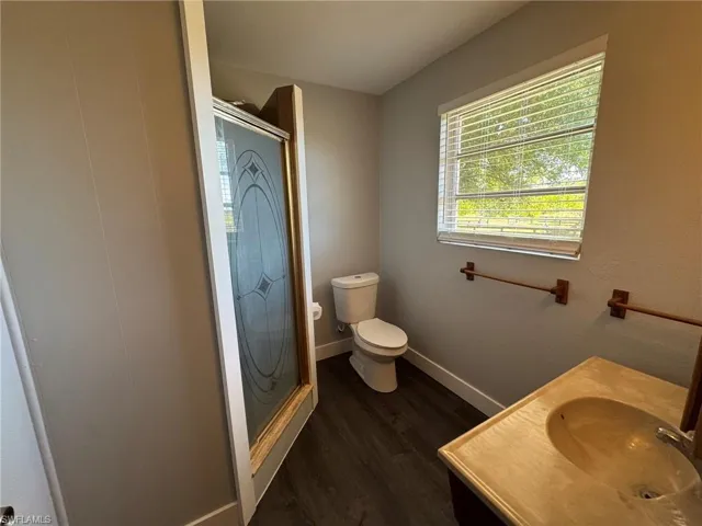 Bathroom with wood finished floors, a shower stall, toilet, and baseboards