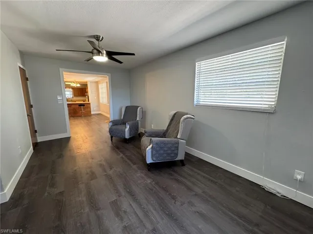 Living area with a ceiling fan, a textured ceiling, baseboards, and dark wood-style flooring