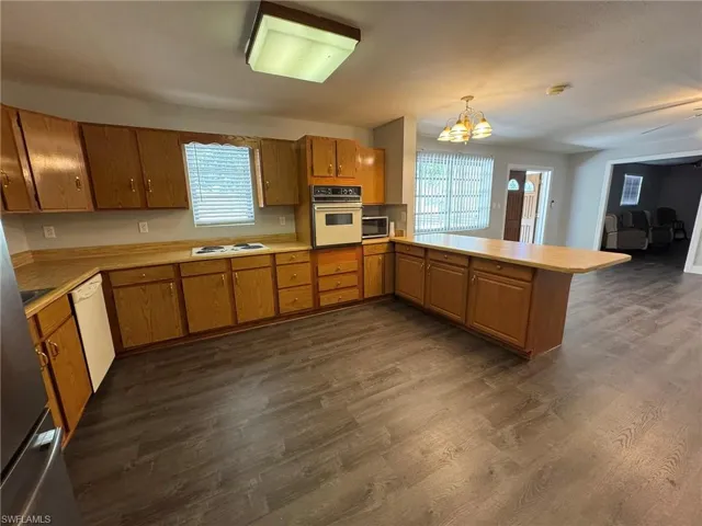 Kitchen with light countertops, hanging light fixtures, brown cabinetry, white appliances, and a peninsula