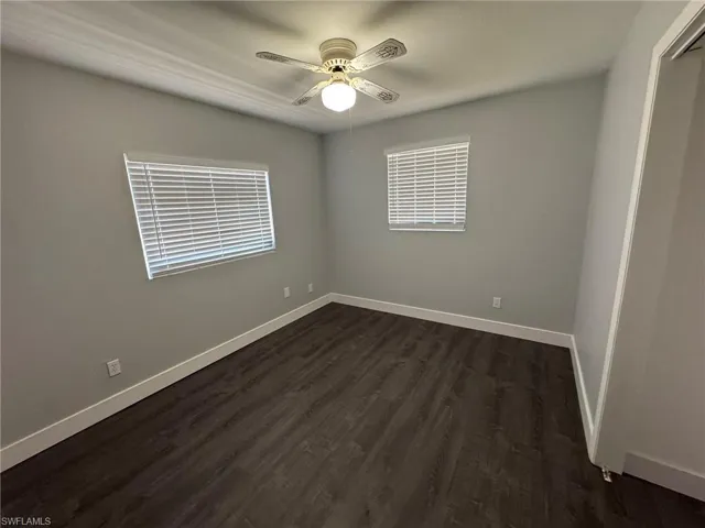 Spare room with dark wood finished floors, a ceiling fan, and baseboards