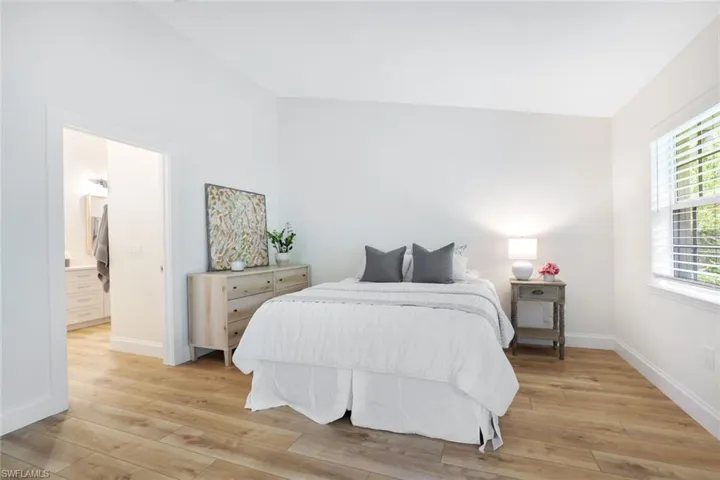 The primary bedroom features a cathedral ceiling, access to the screened lanai, and a view of preserve, as well as the light wood-style flooring seen throughout the entire home