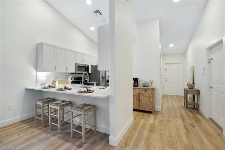 View of kitchen peninsula / breakfast bar and completely renovated kitchen featuring vaulted ceiling, custom wood cabinetry, stainless steel appliances, and beautifully updated wood-style flooring throughout entire home