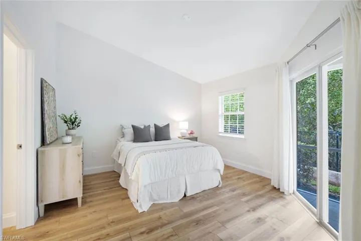 The primary bedroom features a cathedral ceiling, access to the screened lanai, and a view of preserve, as well as the light wood-style flooring seen throughout the rest of the home