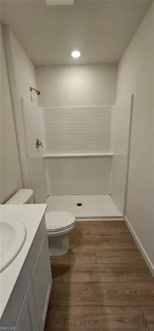 Bathroom featuring a walk-in shower with white subway tile-style surround, wood-finish flooring, white vanity with integrated sink, and recessed lighting