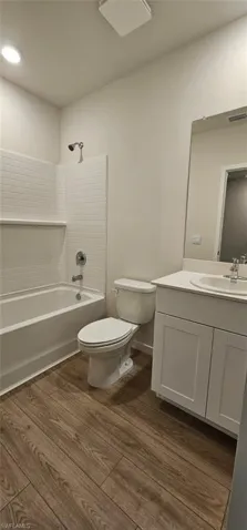Bathroom featuring wood-finish flooring, white vanity with a white countertop, and a bathtub with white subway tile surround