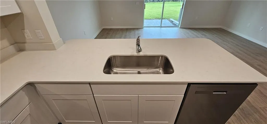 Kitchen island with a stainless steel sink, chrome faucet, light-toned countertop, and white shaker-style cabinetry