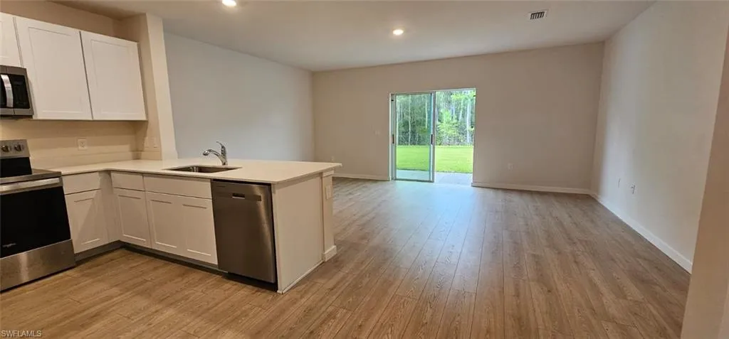 Open-concept living area featuring wood-finish flooring, white cabinetry, stainless steel appliances, and a sliding glass door leading to a backyard