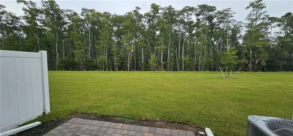Expansive lawn area with a privacy fence, paver patio, and mature tree line