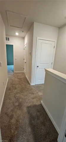 Carpeted hallway with painted walls, white doors, and a ceiling access panel