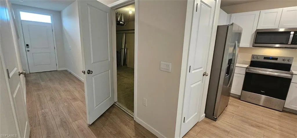 Entryway featuring wood-finish flooring and a kitchen with stainless steel appliances, white cabinetry, and a built-in microwave