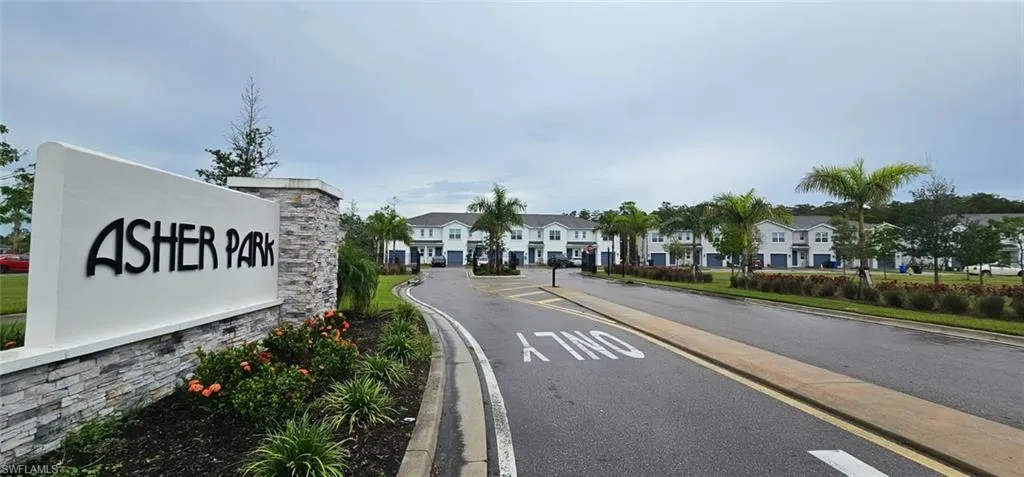 Entryway sign with stone veneer, manicured landscaping, and asphalt paving
