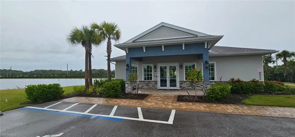Building with gabled roofline, stone veneer accents, double-door entry, and exterior wall sconces, situated beside a body of water