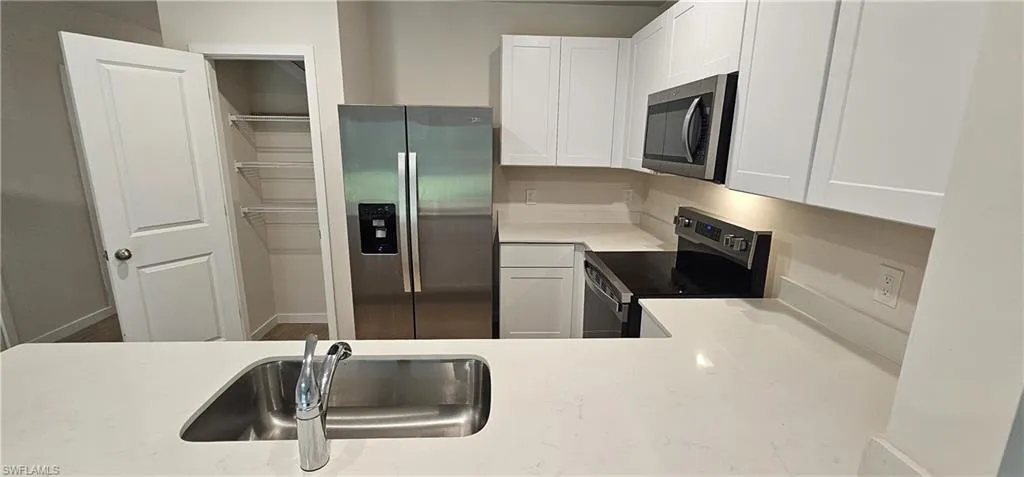 White shaker-style cabinetry, stainless steel appliances, light-toned countertops, integrated sink, and pantry with shelving