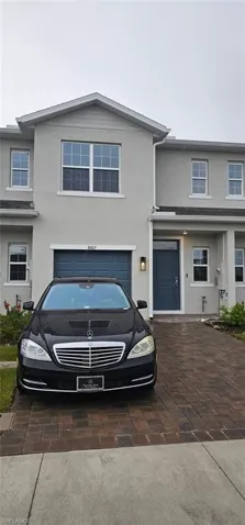 Modern two-story residence featuring a stucco exterior with mixed neutral toning, peaked roofline with gabled detailing, and a two-car garage with blue paneled door
