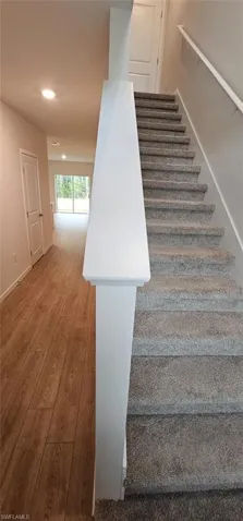 Wood-finish flooring, carpeted staircase, white newel post, recessed lighting, and sliding glass doors