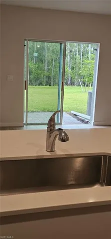 Stainless steel undermount sink with a polished chrome faucet, white countertop, and sliding glass doors opening to a green lawn
