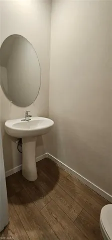 Pedestal sink with chrome faucet, oval wall mirror, and wood-finish plank flooring