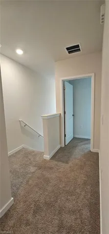 Plush carpeting throughout, featuring a white painted handrail, recessed lighting, and a paneled interior door