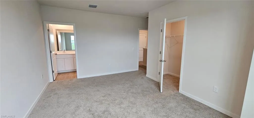Spacious primary bedroom with neutral wall finishes, carpeted flooring, and multiple entry points including access to an ensuite bathroom and walk-in closet
