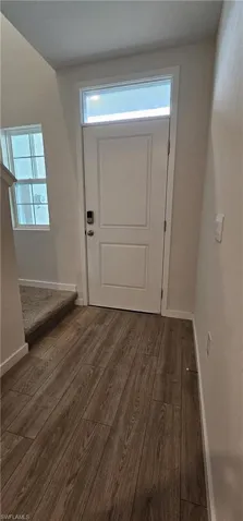 Entryway featuring wood-finish flooring, a white paneled door with transom window, and a carpeted staircase