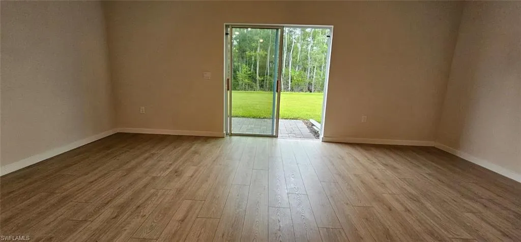 Spacious room with wood-finish flooring throughout and glass French doors opening to outdoor space with mature landscaping