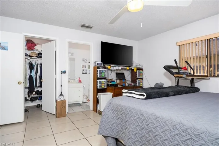 Bedroom with a textured ceiling, a spacious closet, light tile patterned flooring, and ceiling fan