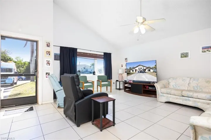 Living area with lofted ceiling, ceiling fan, and light tile patterned floors