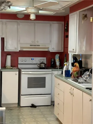 Kitchen featuring white electric range oven, light vinyl flooring, under cabinet range hood, and white cabinetry.