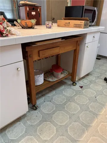 Kitchen view of light flooring, tile countertops, and stainless steel microwave