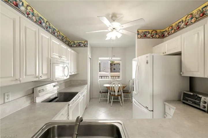 Kitchen with white appliances, a sink, light countertops, a ceiling fan, and white cabinetry