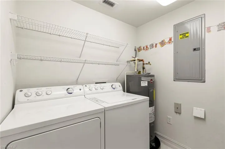 Laundry area featuring electric panel, separate washer and dryer, water heater, and baseboards