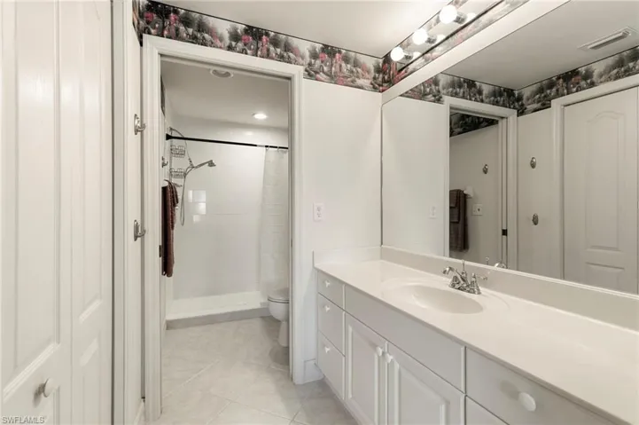 Full bath with toilet, tile patterned floors, vanity, and tiled shower