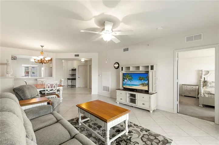 Living room with light tile patterned flooring, a chandelier, a ceiling fan, and baseboards