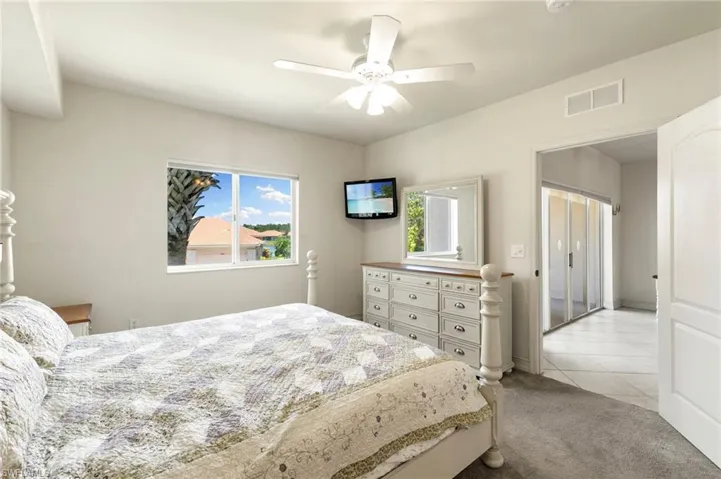 Bedroom with multiple windows, light tile patterned flooring, light colored carpet, and ceiling fan