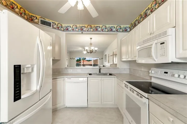 Kitchen featuring white appliances, a sink, ceiling fan, a chandelier, and light tile patterned flooring