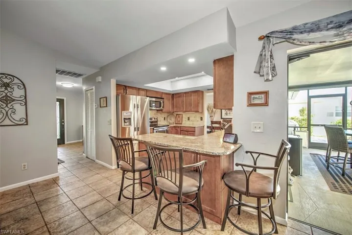 Kitchen featuring kitchen peninsula, appliances with stainless steel finishes, a kitchen bar, tasteful backsplash, and light stone countertops
