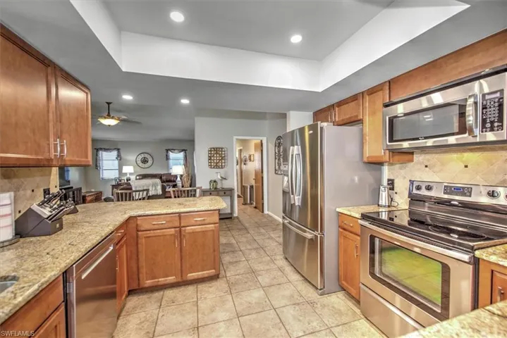 Kitchen featuring decorative backsplash, ceiling fan, light stone countertops, and appliances with stainless steel finishes