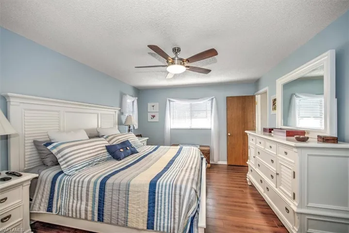 Bedroom with a textured ceiling, ceiling fan, dark wood-type flooring, and multiple windows