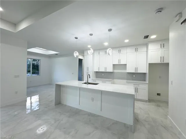 Kitchen with marble finish floor, baseboards, recessed lighting, white cabinetry, and a sink