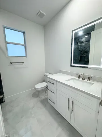 Bathroom featuring vanity, toilet, marble finish floor, baseboards, and visible vents
