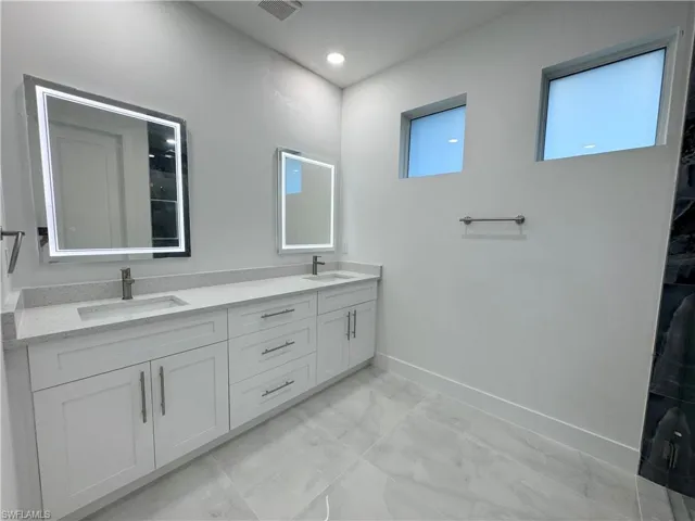 Bathroom featuring baseboards, a sink, marble finish floor, and double vanity