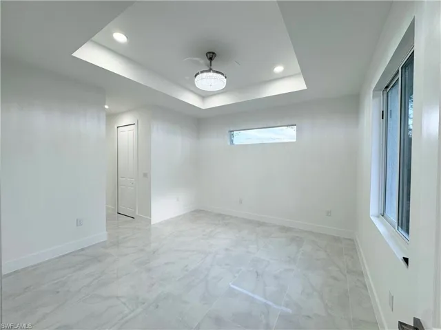Unfurnished room with baseboards, a tray ceiling, recessed lighting, and marble finish floor