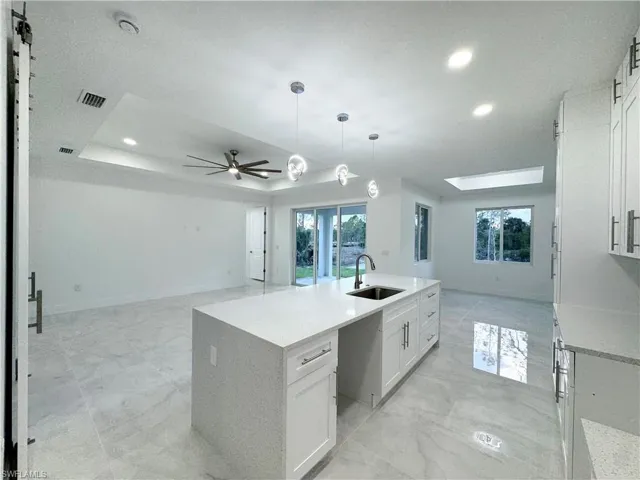 Kitchen with a sink, white cabinetry, open floor plan, visible vents, and a center island with sink